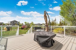 Expansive composite deck featuring glass panel railings, white posts, and steps descending to a landscaped backyard with a manicured lawn - 