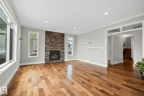 Spacious room featuring wood-finish flooring, a stacked stone fireplace, large windows, recessed lighting, and crown molding - 9 Greenfield Wynd, Fort Saskatchewan, AB - Indoor Photo Showing Living Room With Fireplace