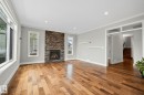 Spacious room featuring wood-finish flooring, a stacked stone fireplace, large windows, recessed lighting, and crown molding - 9 Greenfield Wynd, Fort Saskatchewan, AB  - Indoor Photo Showing Living Room With Fireplace 