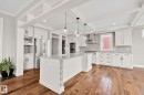 Spacious kitchen featuring an expansive center island with integrated wine storage, white cabinetry, stainless steel appliances, wood-finish flooring, and a coffered ceiling - 9 Greenfield Wynd, Fort Saskatchewan, AB  - Indoor Photo Showing Kitchen With Stainless Steel Kitchen With Upgraded Kitchen 