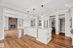 Open-concept living space featuring wood-finish flooring, a central kitchen island with seating space, stainless steel appliances, a stone-faced fireplace, and recessed lighting throughout - 