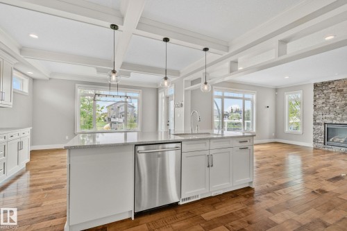 Kitchen island with a stainless steel dishwasher, undermount sink, and light-toned countertop - 9 Greenfield Wynd, Fort Saskatchewan, AB - Indoor Photo Showing Kitchen With Fireplace