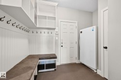 Mudroom featuring built-in white cabinetry, integrated bench seating with storage below, extensive wall hooks, and dark tile flooring - 