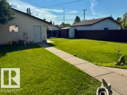 Spacious backyard featuring a detached garage with a white entry door, a privacy fence, and a concrete pathway - 