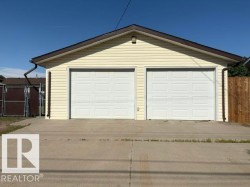 Detached two-car garage with light yellow siding, white panel garage doors, and a brown shingle roof - 