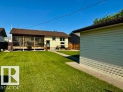 Expansive green lawn with a screened-in back porch, concrete walkway, and a detached structure featuring horizontal siding - 
