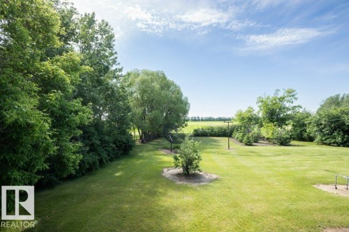 Expansive green lawn surrounded by mature trees and shrubs, offering open fields in the background - 25023 Twp Rd 612, Rural Westlock County, AB 