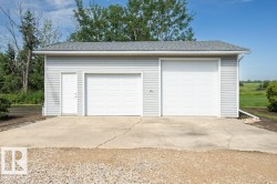 Detached two-car garage with light gray siding, white paneled garage doors, and a side entry door - 