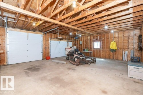 Spacious garage featuring two overhead doors, exposed wood beam ceiling, concrete flooring, and a single window - 25023 Twp Rd 612, Rural Westlock County, AB 