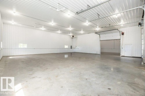 Spacious industrial interior featuring a concrete floor, bright overhead lighting, white corrugated metal walls, and multiple bay doors - 25023 Twp Rd 612, Rural Westlock County, AB 