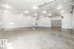 Spacious industrial interior featuring a concrete floor, bright overhead lighting, white corrugated metal walls, and multiple bay doors - 