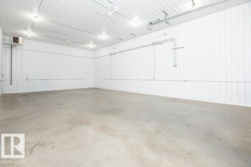 Spacious interior featuring a concrete floor, corrugated metal walls, exposed conduit, surface-mounted lighting, and a wall-mounted ventilation unit - 25023 Twp Rd 612, Rural Westlock County, AB 