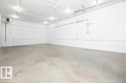 Spacious interior featuring a concrete floor, corrugated metal walls, exposed conduit, surface-mounted lighting, and a wall-mounted ventilation unit - 