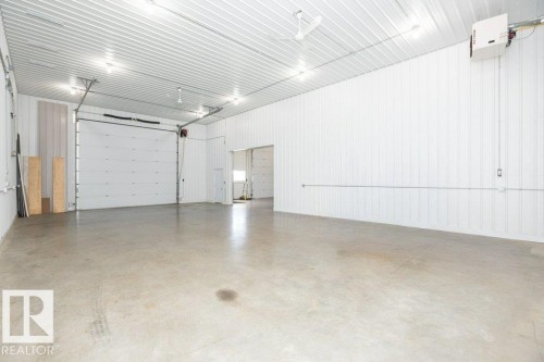 Spacious industrial interior featuring a large roll-up door, exposed corrugated metal ceiling, concrete flooring, and bright overhead lighting - 25023 Twp Rd 612, Rural Westlock County, AB 