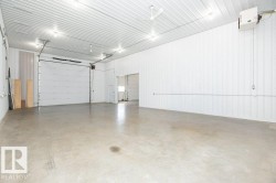 Spacious industrial interior featuring a large roll-up door, exposed corrugated metal ceiling, concrete flooring, and bright overhead lighting - 
