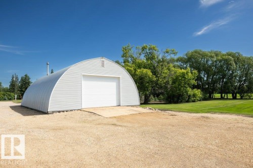Quonset-style outbuilding featuring a corrugated metal exterior, large white roll-up door, and a gravel approach - 25023 Twp Rd 612, Rural Westlock County, AB 