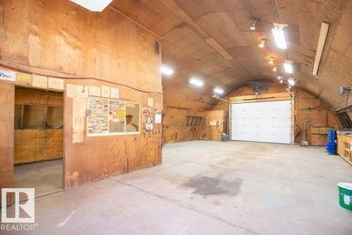 Spacious workshop structure featuring a large overhead door, concrete flooring, exposed plywood walls, and overhead lighting - 25023 Twp Rd 612, Rural Westlock County, AB 