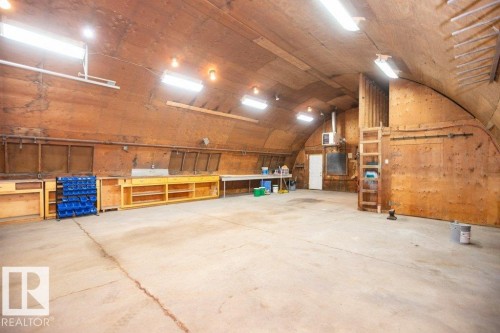 Expansive workspace featuring an arched plywood ceiling, concrete flooring, built-in shelving, integrated workbenches, and overhead fluorescent lighting - 25023 Twp Rd 612, Rural Westlock County, AB 