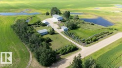 Expansive property featuring multiple structures, including a primary residence with a white roof, a large workshop with a grey roof, and two additional outbuildings - 