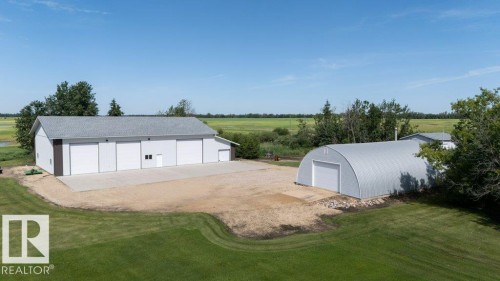 Large white outbuilding with multiple garage doors, a concrete pad, and a separate metal Quonset hut - 25023 Twp Rd 612, Rural Westlock County, AB 