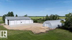 Large white outbuilding with multiple garage doors, a concrete pad, and a separate metal Quonset hut - 