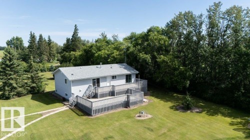 Light grey siding exterior with a large multi-level wood deck, a winding stone pathway, and extensive surrounding greenery - 25023 Twp Rd 612, Rural Westlock County, AB 