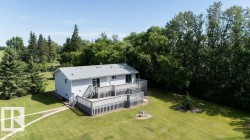 Light grey siding exterior with a large multi-level wood deck, a winding stone pathway, and extensive surrounding greenery - 
