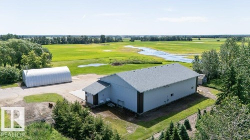 Expansive property featuring a large light-colored commercial-style building with a dark-trimmed base, an additional quonset hut structure, and surrounding green landscapes with mature trees - 25023 Twp Rd 612, Rural Westlock County, AB 