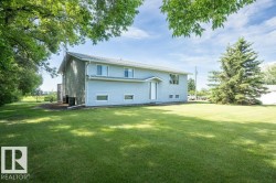 Spacious lot featuring a large grassy area, mature trees, and a two-story residence with light blue siding and white trim - 