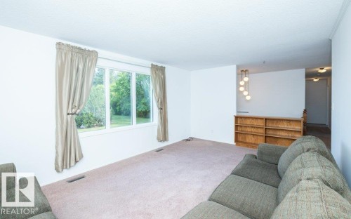 Bright living area featuring a large window, light-toned carpeting, and a built-in wooden shelving unit - 25023 Twp Rd 612, Rural Westlock County, AB 