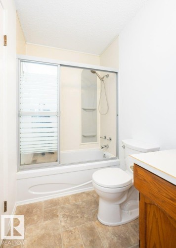 Bathroom featuring a tub/shower combination with sliding glass enclosure, a white toilet, and a wood-finish vanity with a light-colored countertop - 25023 Twp Rd 612, Rural Westlock County, AB 