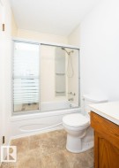 Bathroom featuring a tub/shower combination with sliding glass enclosure, a white toilet, and a wood-finish vanity with a light-colored countertop - 