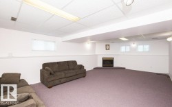 Spacious room featuring broadloom carpeting, a corner-set fireplace with a raised hearth, and multiple windows providing natural light - 
