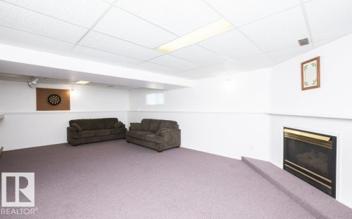 Spacious recreation room featuring lavender carpeting, a built-in fireplace with a gold-tone trim, white walls, and a drop ceiling with recessed lighting - 25023 Twp Rd 612, Rural Westlock County, AB 