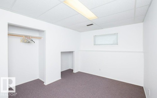 Carpeted room featuring a drop ceiling with fluorescent lighting, built-in open closet with shelving and hanging rod, and a wall cut-out - 25023 Twp Rd 612, Rural Westlock County, AB 