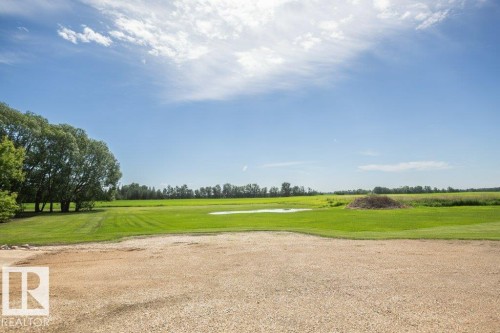 Expansive natural landscape featuring a gravel foreground, a broad green lawn, a cluster of mature trees, a small body of water, and distant foliage - 25023 Twp Rd 612, Rural Westlock County, AB 