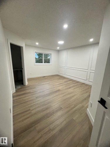 Spacious room featuring wood-finish flooring, a contemporary accent wall with panel molding, and white trim throughout - 3320 43 Street, Edmonton, AB 