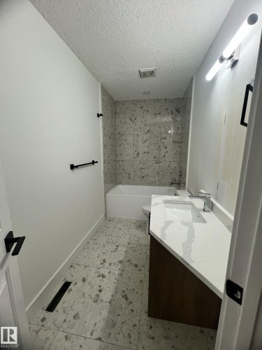 Bathroom featuring a white bathtub with a tiled surround, a toilet, and a wood-finish vanity with a white countertop and integrated sink - 3320 43 Street, Edmonton, AB 