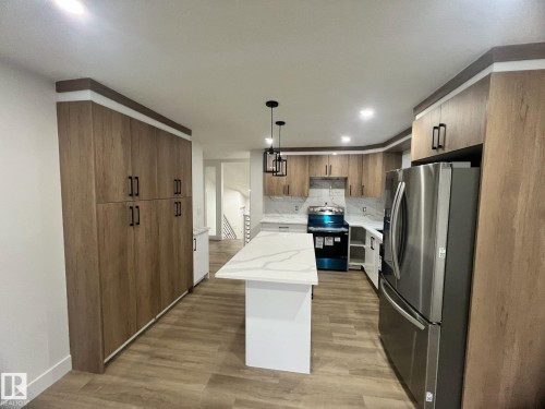 Kitchen featuring wood-finish cabinetry, stainless steel refrigerator, white quartz countertops, and coordinating backsplash - 3320 43 Street, Edmonton, AB 