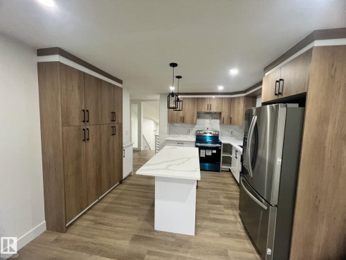 Modern kitchen featuring extensive wood-finish cabinetry, a white quartz island, stainless steel appliances, and wood-finish flooring - 3320 43 Street, Edmonton, AB 
