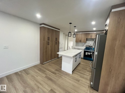 Modern kitchen featuring a central island with a light-toned countertop, wood-finish flooring, recessed lighting, and pendant lighting fixtures - 3320 43 Street, Edmonton, AB 