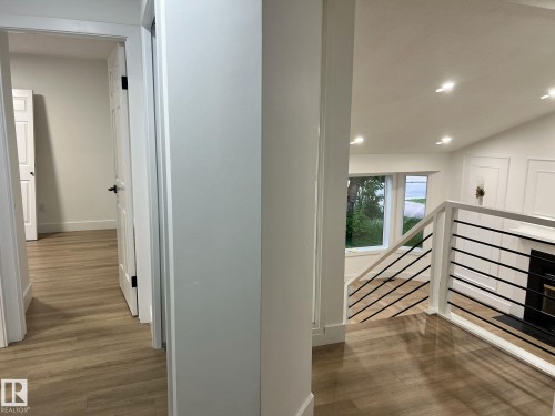 Contemporary interior featuring wood-finish flooring throughout, a modern railing with black balusters, recessed lighting, and white paneled walls - 3320 43 Street, Edmonton, AB 