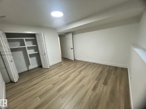 Room with wood-finish flooring, a built-in closet with shelving, a white paneled door, and a circular ceiling light fixture - 3320 43 Street, Edmonton, AB 