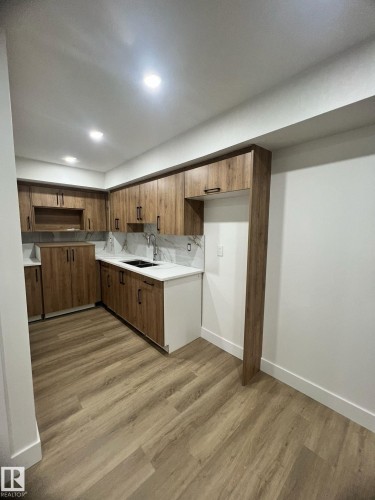 Modern kitchen featuring wood-finish cabinetry with matte black hardware, white countertops, and a full-height tile backsplash - 3320 43 Street, Edmonton, AB 