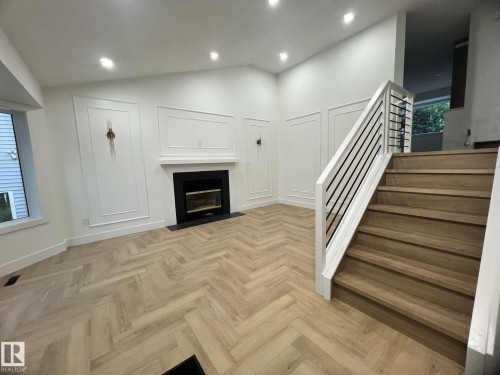 Living area featuring herringbone wood-finish flooring, a fireplace with a black surround and hearth, and decorative wall paneling - 3320 43 Street, Edmonton, AB 