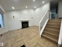Living area featuring herringbone wood-finish flooring, a fireplace with a black surround and hearth, and decorative wall paneling - 3320 43 Street, Edmonton, AB 