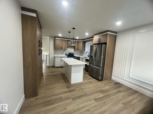 Kitchen featuring a central island with a white countertop, stainless steel appliances, wood-finish cabinetry, and recessed lighting - 3320 43 Street, Edmonton, AB 