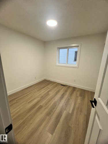 Bright room featuring wood-finish flooring, white baseboards, a white window frame, and a flush-mount ceiling light fixture - 3320 43 Street, Edmonton, AB 