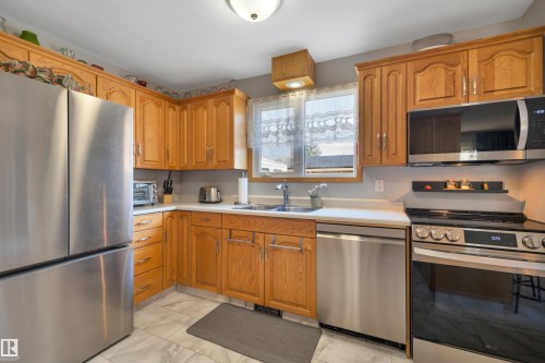 Kitchen featuring wood cabinetry, stainless steel appliances, white countertops, a double basin sink, and tile flooring - 184 Garwood Cres, Wetaskiwin, AB - Indoor Photo Showing Kitchen With Double Sink