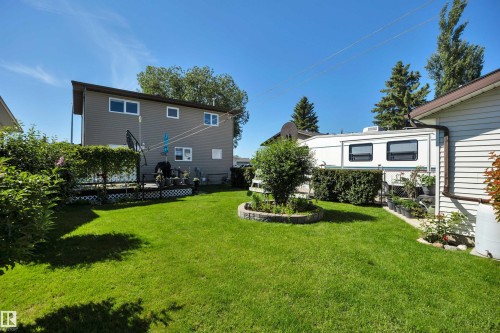 Expansive rear yard featuring a manicured lawn, a built-in planter with stone surround, and mature perimeter landscaping - 184 Garwood Cres, Wetaskiwin, AB - Outdoor
